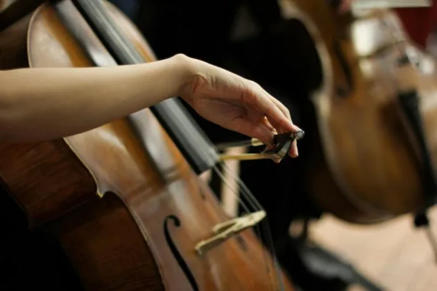 An artistic close-up of a person playing a cello, focusing on the bow and strings.