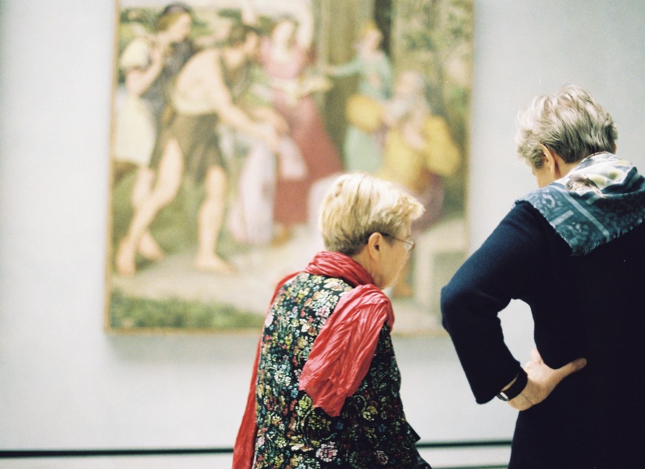 Two senior women admire a painting in an art museum, showcasing appreciation for fine art.
