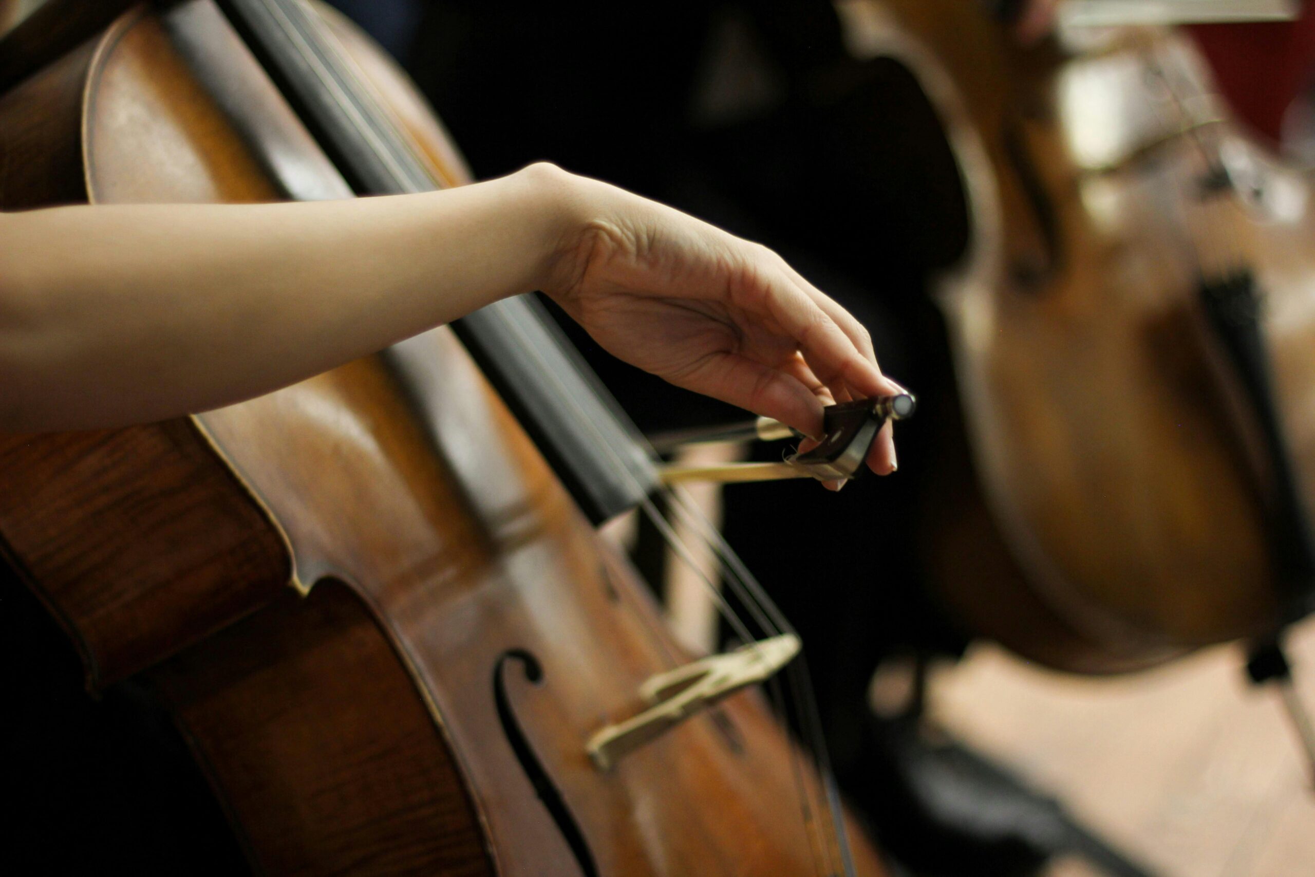 An artistic close-up of a person playing a cello, focusing on the bow and strings.